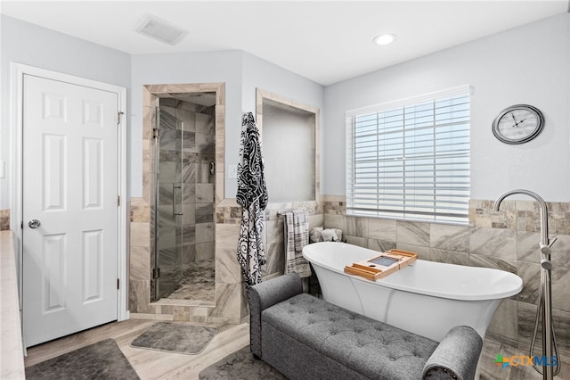 bathroom featuring visible vents, tile walls, a soaking tub, wood finished floors, and a stall shower