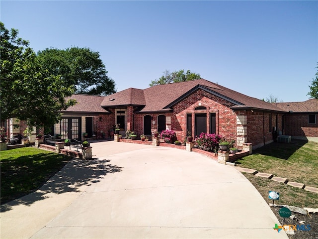 ranch-style house with central AC unit, a shingled roof, brick siding, french doors, and a front lawn