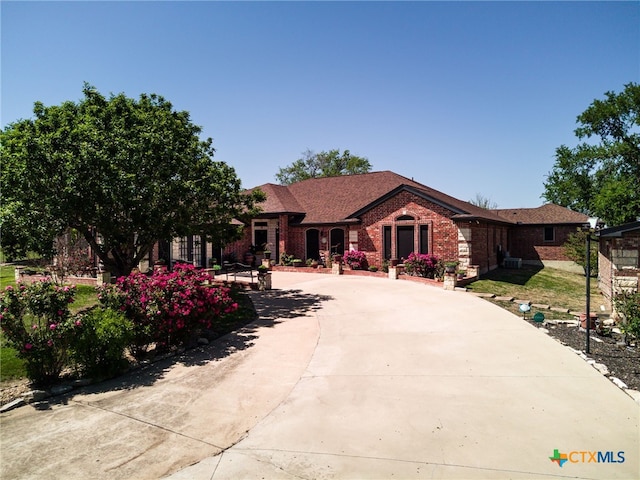 ranch-style home featuring brick siding, curved driveway, and roof with shingles