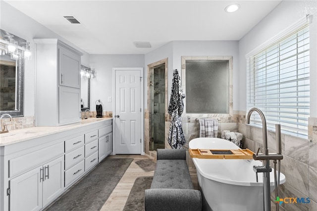 bathroom with a shower stall, a freestanding tub, visible vents, a sink, and tile walls