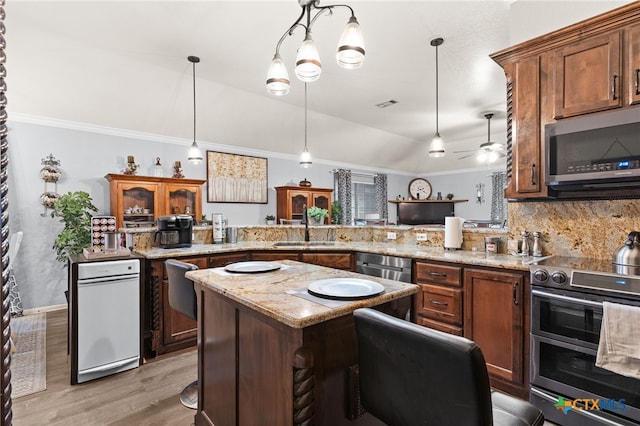 kitchen featuring a peninsula, appliances with stainless steel finishes, a sink, decorative light fixtures, and light wood finished floors