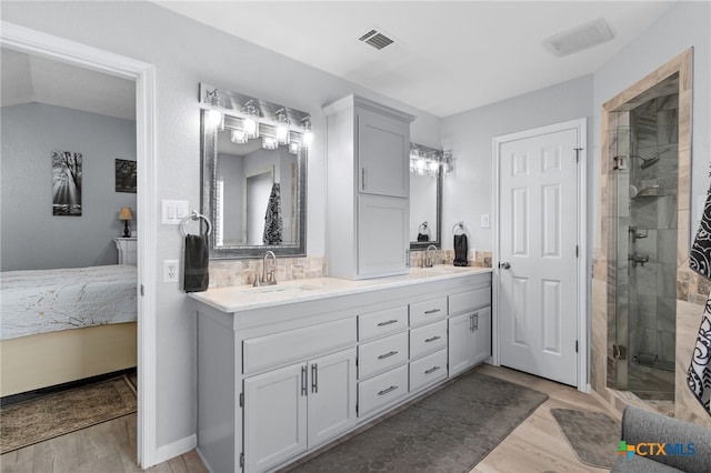 ensuite bathroom with double vanity, a stall shower, visible vents, a sink, and wood finished floors