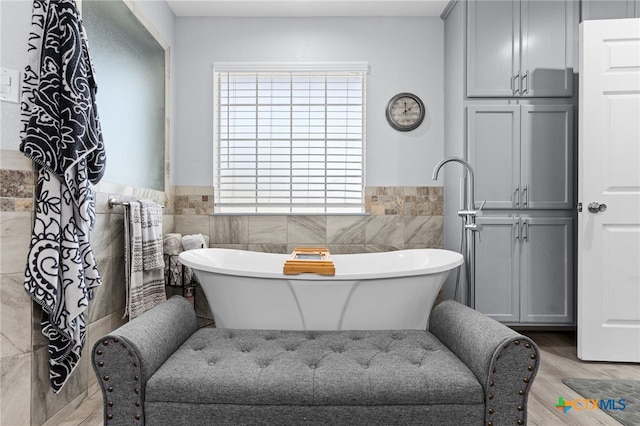 full bath featuring a wainscoted wall, tile walls, a freestanding bath, and wood finished floors
