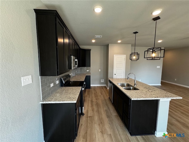 kitchen with a center island with sink, sink, appliances with stainless steel finishes, backsplash, and decorative light fixtures