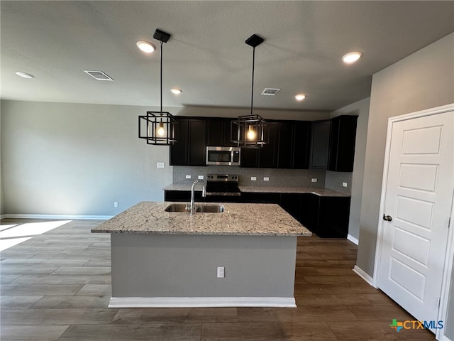 kitchen featuring stainless steel appliances, light stone countertops, hanging light fixtures, sink, and a kitchen island with sink