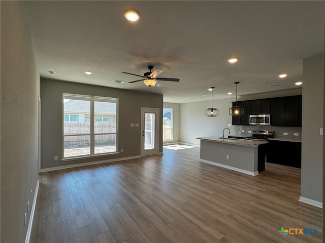 kitchen featuring hardwood / wood-style flooring, a kitchen island with sink, ceiling fan, appliances with stainless steel finishes, and decorative light fixtures