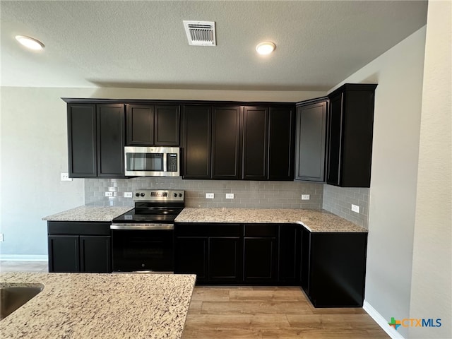 kitchen with light stone countertops, appliances with stainless steel finishes, decorative backsplash, and light hardwood / wood-style floors