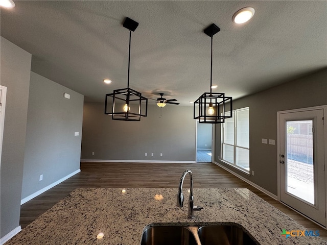 kitchen with dark wood-type flooring, sink, light stone countertops, and decorative light fixtures