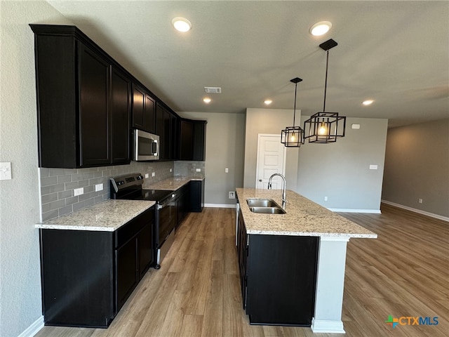 kitchen featuring stainless steel appliances, sink, hanging light fixtures, a kitchen island with sink, and light wood-type flooring