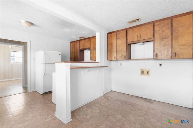 1202 S 3rd St, Copperas Cove, TX 76522 - kitchen featuring freestanding refrigerator, brown cabinets, a textured ceiling, and a peninsula