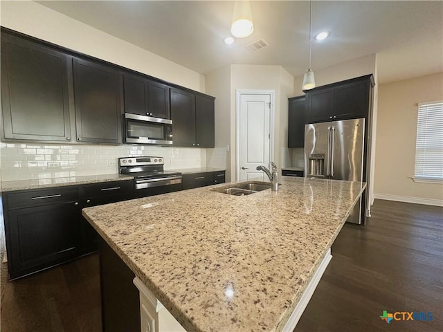 kitchen with decorative light fixtures, sink, a kitchen island with sink, stainless steel appliances, and light stone counters