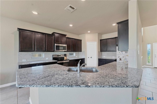 kitchen with a large island, sink, stainless steel appliances, light stone counters, and backsplash