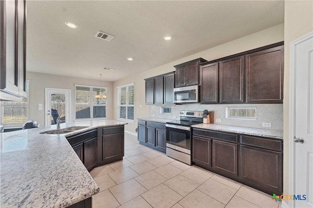 kitchen with decorative backsplash, appliances with stainless steel finishes, light stone counters, sink, and light tile patterned floors