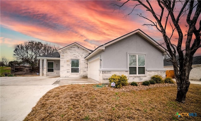 view of front of house with stucco siding, stone siding, fence, a yard, and an attached garage