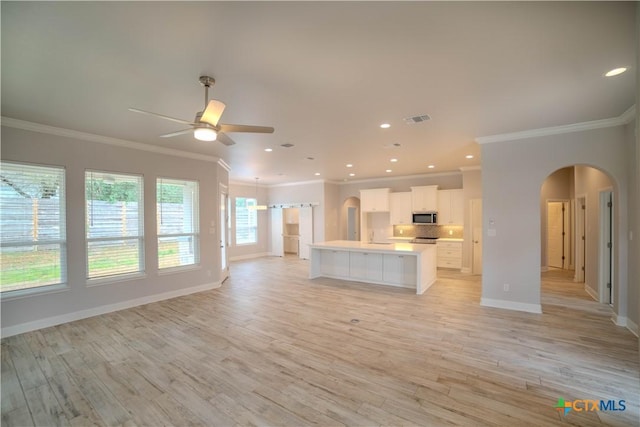 kitchen featuring visible vents, stainless steel microwave, open floor plan, arched walkways, and decorative backsplash