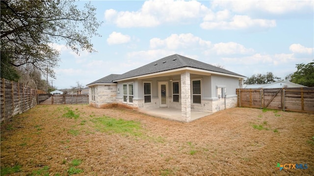 back of house featuring stone siding, a yard, a patio, and a fenced backyard