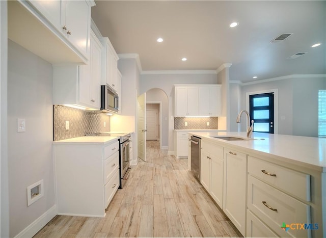 kitchen with light countertops, light wood-type flooring, appliances with stainless steel finishes, arched walkways, and a sink