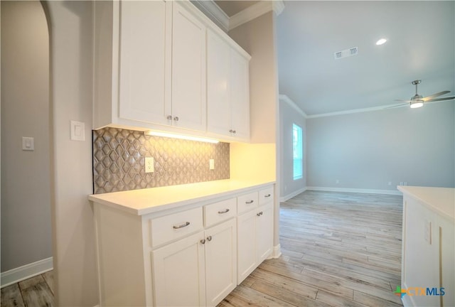 kitchen with visible vents, ornamental molding, light wood finished floors, decorative backsplash, and light countertops