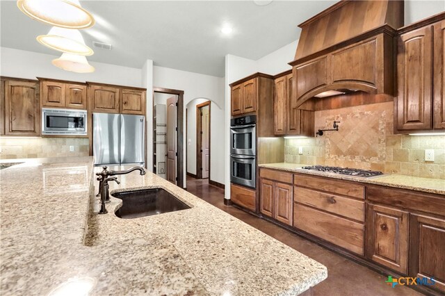 kitchen featuring tasteful backsplash, stainless steel appliances, decorative light fixtures, light stone countertops, and sink