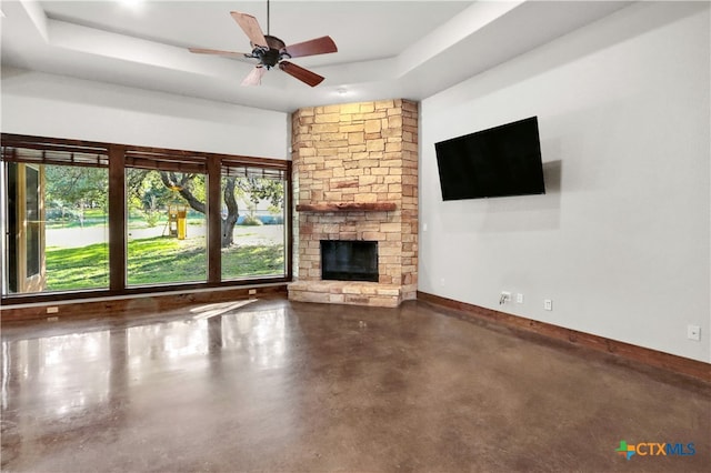 unfurnished living room featuring a stone fireplace, ceiling fan, and a raised ceiling