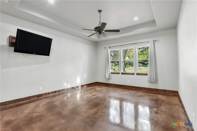 spare room with concrete flooring, ceiling fan, and a raised ceiling