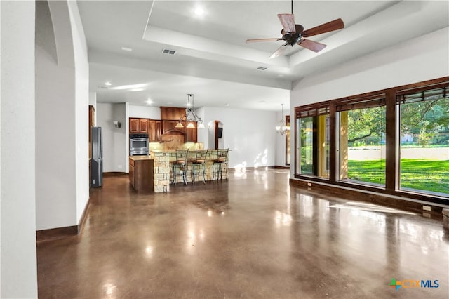 living room with a tray ceiling and ceiling fan with notable chandelier