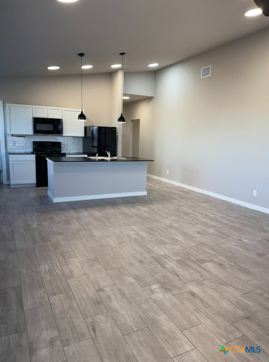 kitchen featuring an island with sink, decorative light fixtures, decorative backsplash, white cabinets, and black appliances