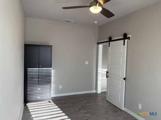 unfurnished room with ceiling fan, a barn door, and dark wood-type flooring