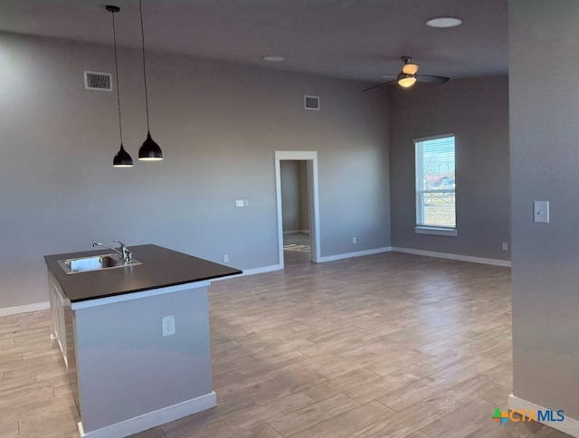 kitchen featuring ceiling fan, sink, light hardwood / wood-style flooring, hanging light fixtures, and an island with sink