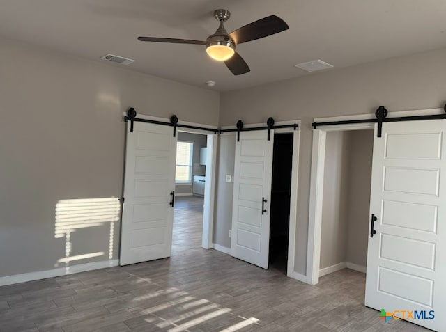 unfurnished bedroom featuring ceiling fan, a barn door, and light wood-type flooring