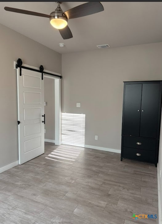 unfurnished bedroom featuring a barn door and ceiling fan