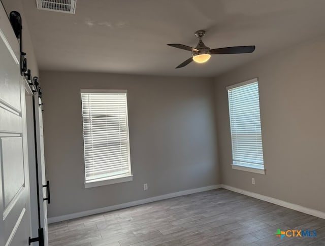 spare room with light wood-type flooring, a barn door, and ceiling fan