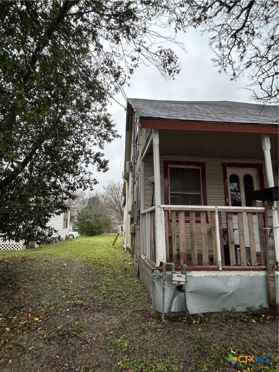 view of side of home featuring covered porch, roof with shingles, and a yard