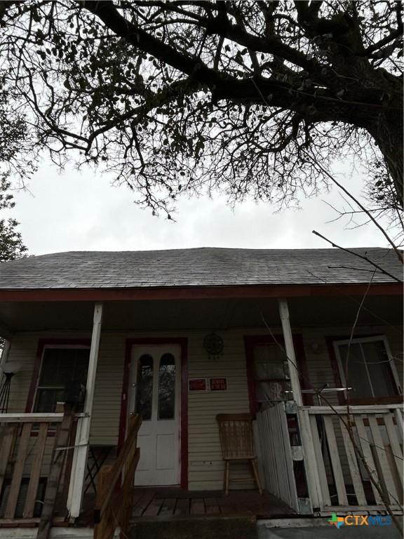 entrance to property with covered porch and roof with shingles