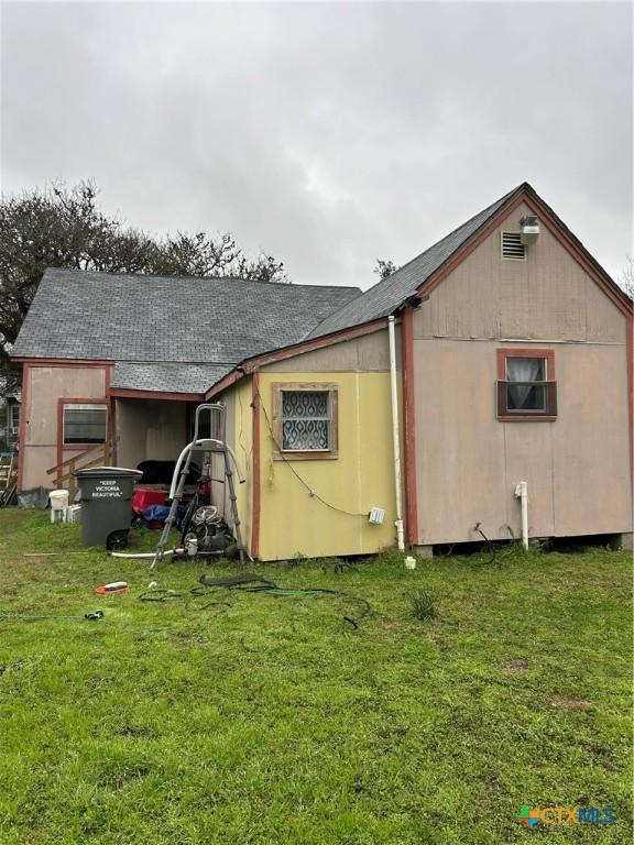 back of house featuring a lawn and roof with shingles