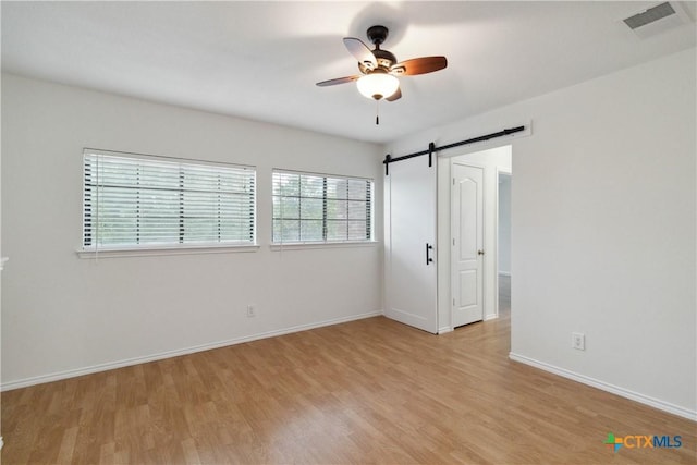 unfurnished bedroom with multiple windows, ceiling fan, light hardwood / wood-style floors, and a barn door