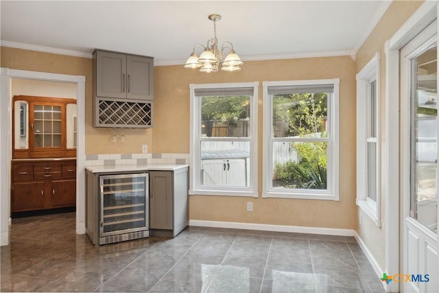 bar featuring gray cabinetry, hanging light fixtures, wine cooler, a notable chandelier, and ornamental molding