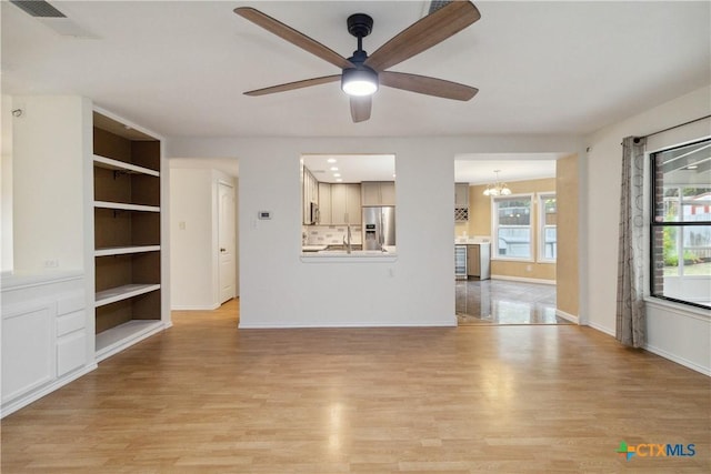 unfurnished living room with ceiling fan with notable chandelier, light hardwood / wood-style floors, sink, and built in features