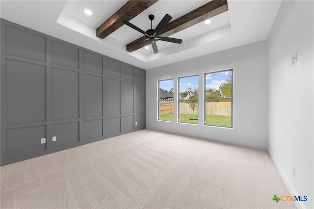 carpeted empty room with a tray ceiling, ceiling fan, and beam ceiling