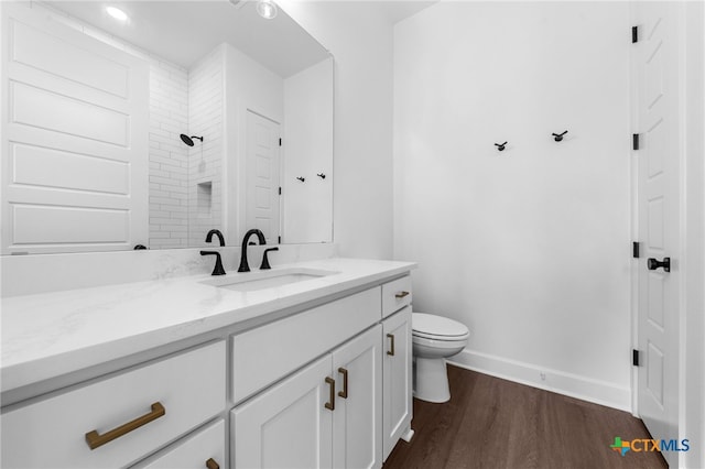 bathroom featuring hardwood / wood-style floors, vanity, toilet, and tiled shower