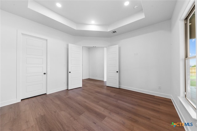 unfurnished bedroom featuring dark hardwood / wood-style flooring and a tray ceiling