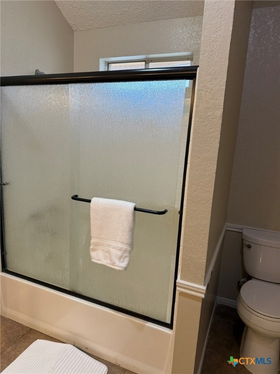 bathroom with toilet, bath / shower combo with glass door, a textured ceiling, and tile patterned flooring