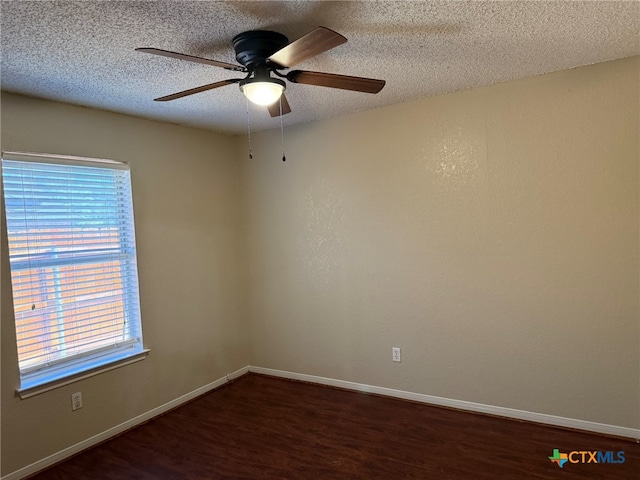 empty room with a wealth of natural light, dark wood-type flooring, and a textured ceiling