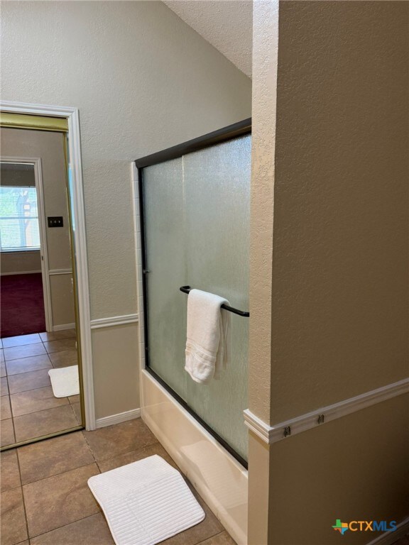 bathroom with bath / shower combo with glass door and tile patterned floors