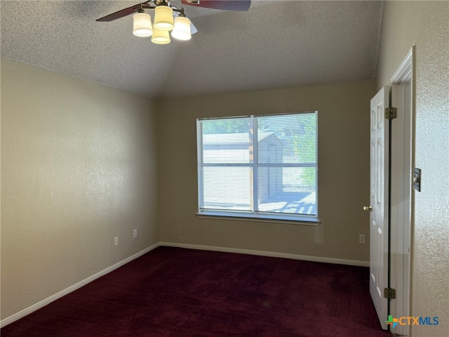 spare room with a textured ceiling, dark colored carpet, ceiling fan, and vaulted ceiling