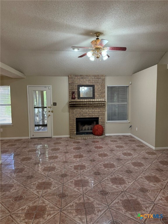 unfurnished living room with a fireplace, ceiling fan, and a textured ceiling