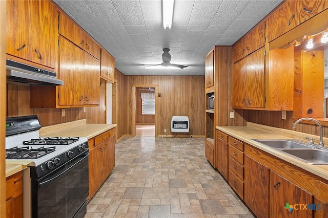 kitchen featuring range with gas cooktop, ceiling fan, wood walls, sink, and heating unit