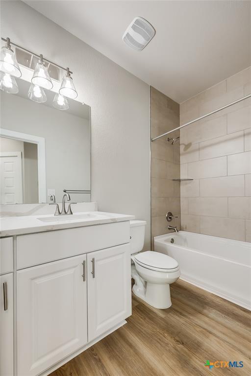 full bathroom featuring tiled shower / bath combo, toilet, wood-type flooring, and vanity