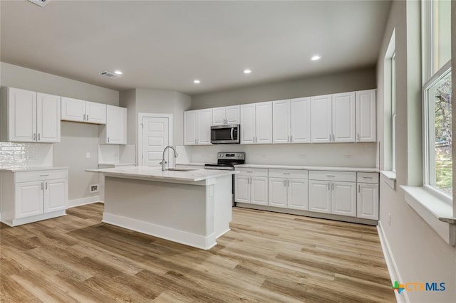 kitchen with appliances with stainless steel finishes, white cabinetry, a kitchen island with sink, and sink