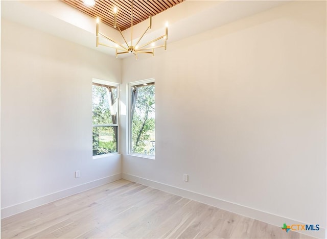 spare room with light wood finished floors, an inviting chandelier, and baseboards